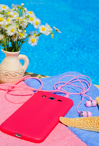 A vase with daisies, a starfish, a mobile phone and headphones on the background of a blue pool. On a summer sunny day.