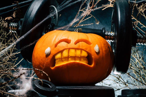 istock Halloween gym concept with carved pumpkin lifting dumbbells. 1434763567