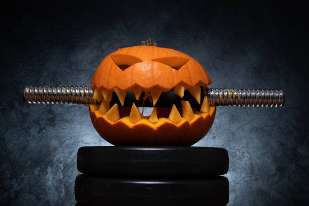 istock Halloween pumpkin clenching teeth on gym barbell dumbbell. 1434763717