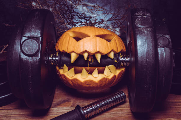 istock Halloween pumpkin clenching teeth on gym barbell dumbbell. 1434763737