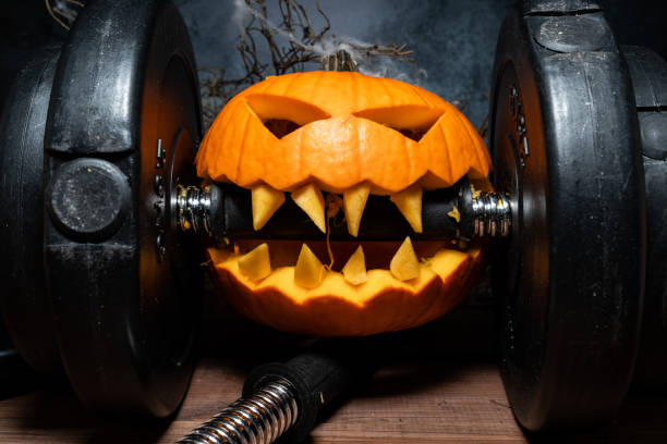 istock Halloween pumpkin clenching teeth on gym barbell dumbbell. 1434763810