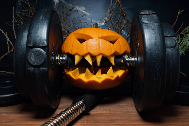 istock Halloween pumpkin clenching teeth on gym barbell dumbbell. 1434763844