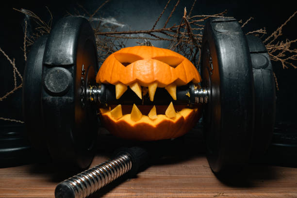 istock Halloween pumpkin clenching teeth on gym barbell dumbbell. 1434763877
