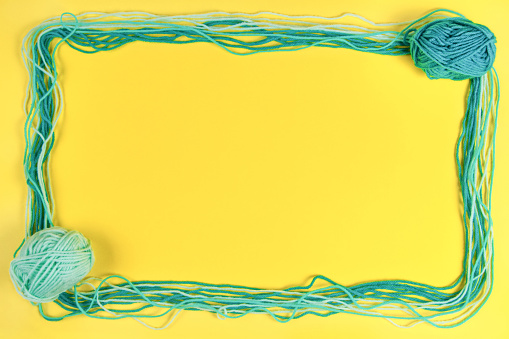 Knitting background. Creative frame made from light green color yarn threads on yellow background. Top view, copy space for text.