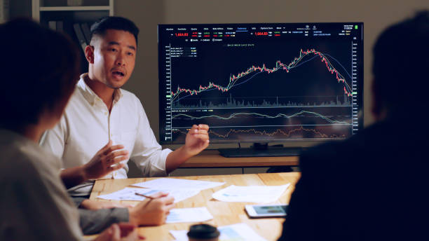 Asian businessman talking about stock market investment and graph from tv screen with broker trader, giving money plan management and analysis stock photo