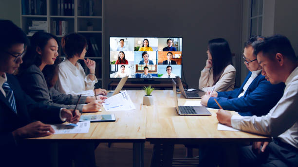 Business people group remote meeting with colleagues via video call conference virtual meeting on tv screen in office at night stock photo