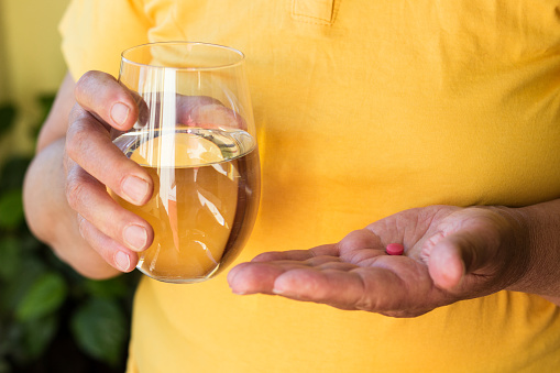 Senior woman hand with pills medicine tablets and glass of water