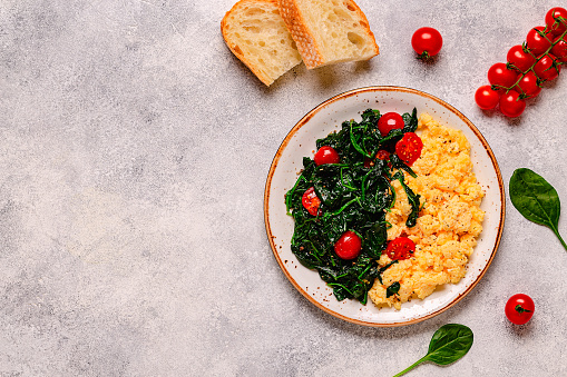 Cooked omelette and spinach with tomatoes on a light background, top view.