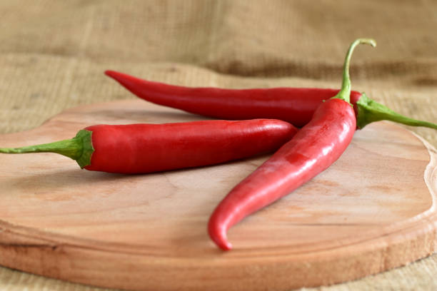 Three pods of red hot chili pepper lie on a cutting board.