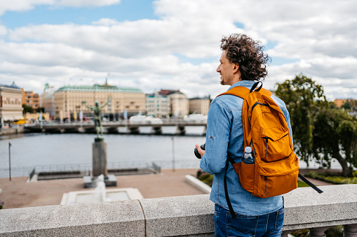Handsome young man holding a camera on the quayside in Stockholm, Sweden.