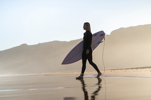 Beautiful surfer girl at the beach standing with her surfboard at sunset time. Female surfer