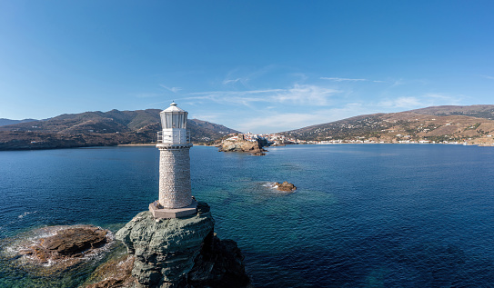 Andros Island. Greece. The stone lighthouse on a rock aerial drone view. Chora town and rocky Cyclades landscape. Blue sky and sea