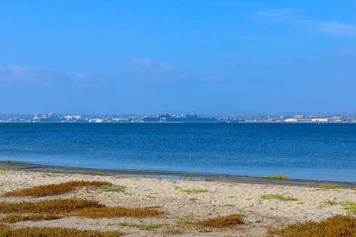 US Navy shipyard in San Diego bay with calm blue water and tan sand shore with brown grass