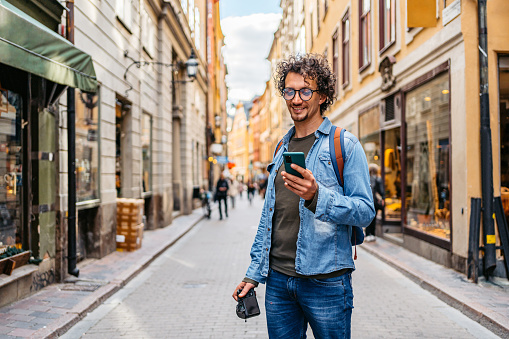 Handsome young tourist using a map on a smart phone in Stockholm, Sweden.