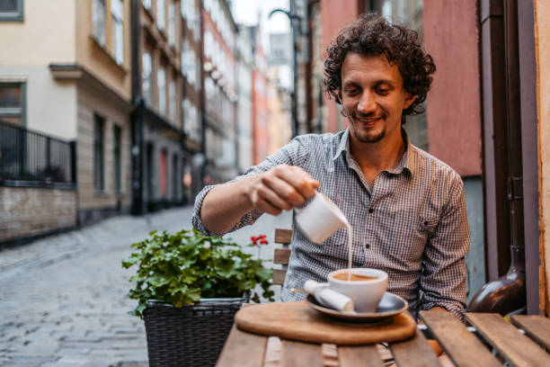 młody człowiek wlewający mleko do kawy w kawiarni na chodniku - sidewalk cafe cafe stockholm sweden zdjęcia i obrazy z banku zdjęć