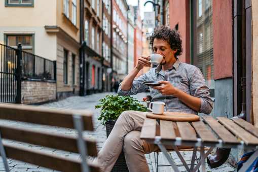 Handsome young man drinking coffee in a sidewalk café in Stockholm, Sweden.