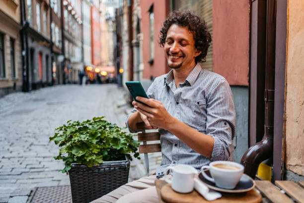 młody człowiek pijący kawę i korzystający z telefonu w kawiarni na chodniku - sidewalk cafe cafe stockholm sweden zdjęcia i obrazy z banku zdjęć