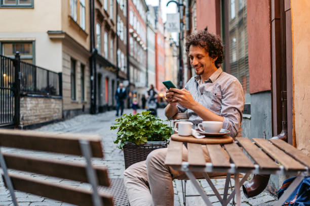 młody człowiek pijący kawę i korzystający z telefonu w kawiarni na chodniku - sidewalk cafe cafe stockholm sweden zdjęcia i obrazy z banku zdjęć