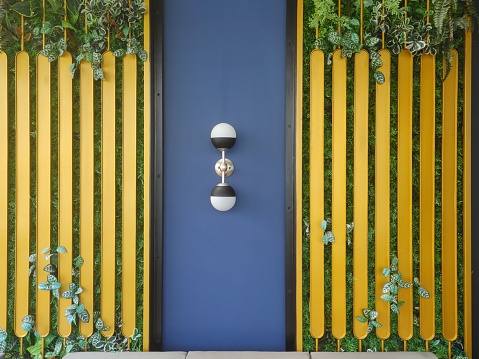 A modern wall with a lamp on the blue background between the yellow fence