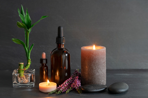 Beauty still life with oils, candles, bamboo and stones, slate background. Spa concept, relaxation, skin care.