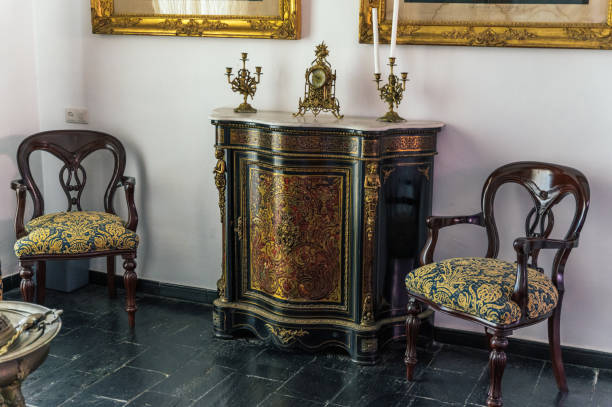 Comfortable antique chairs located near ornamental cabinet with retro candlesticks and clock in light room.