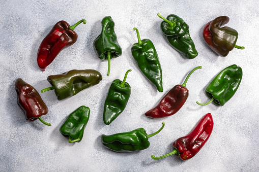 Poblano chile peppers atop grey textured backdrop, top view. Red and green ancho chilies. Capsicum annuum fruits