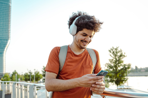 Shot of a young smiling man using a smart phone and relaxing in the city
