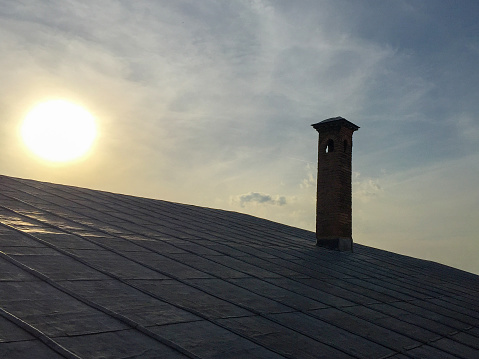 Old building metallic roof and chimney with sun and sky background