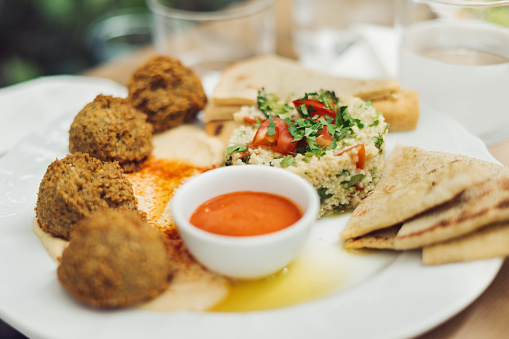 Falafel balls, hummus, quinoa salad, hot harissa sauce and Greek bread. Vegan meal in white plate. Horizontal photo.