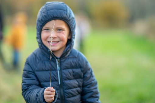 A young school aged boy stands in the grass as he poses for a portrait.  He is dressed warmly in layers and is smiling as he enjoys the crisp fall air.