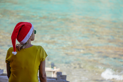 woman with christmas hat in a cave in the sea in an island. Christmas holidays. rear view