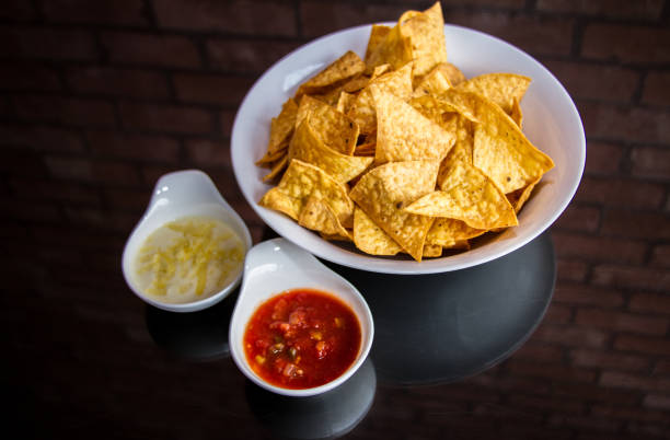Golden crispy potato chips served with tomato sauce on a wooden table, appetizing snack concept.