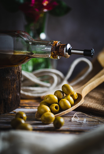 close-up photo of a bottle of virgin olive oil next to a wooden spoon with organic and natural olives