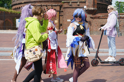 Kaliningrad, Russia - June 19, 2022: Townscape in the sunny summer day. Beautiful young women put on anime cosplay. Ganyu, Yae Miko, Keqing heroes. Friendly walking concept.