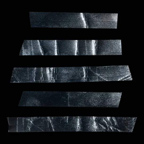 Photo of Metallic sticky teared tape shapes cuts isolated on black background.
