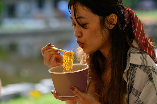 Shot of young Asian Chinese woman enjoy her breakfast instant noodles at campsite early morning.