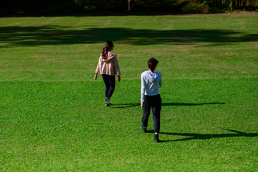 Two Asian women walking in the green field.