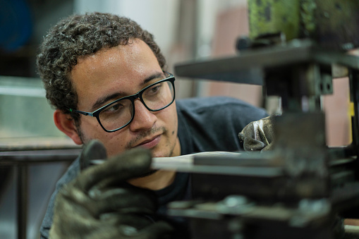 Latino man with an average age of 20 dressed casually Employees of a locksmith are working together cutting metal material