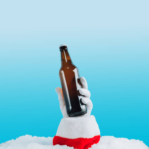 Santa's hand sticking out of a snowdrift and holding a bottle of beer against light blue bokeh background. Santa's hand sticking out of a snowdrift and holding a bottle of beer against light blue bokeh background. Selective focus glass medicine blue bottle stock pictures, royalty-free photos & images