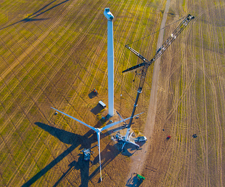 Crew replacing rotor blade assembly on giant wind turbine, Aerial view. The huge scale of these machines is amazing. The human technicians on the ground are about the size of ants by comparison.