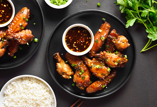 Sticky honey-soy chicken wings on plate over dark stone background. Top view, flat lay, close up