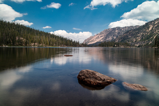 Imogene Lake, a large alpine lake in Idaho's Sawtooth Mountains and within the Sawtooth Wilderness. Seen on a summer day with blue sky and white clouds reflected in the water's surface.