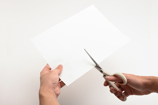Hand holding and cutting white paper with scissors on the white background