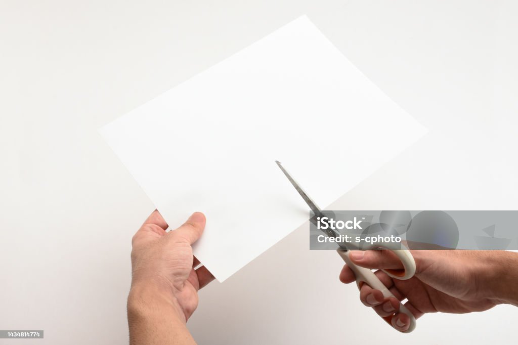 Cutting white paper with scissors Hand holding and cutting white paper with scissors on the white background Cutting Stock Photo