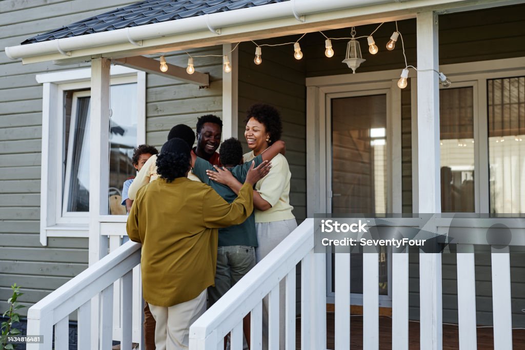 Black Family Embracing By House Portrait of happy black family embracing while standing on porch of new house, copy space Home Ownership Stock Photo