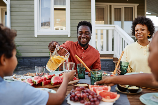 Portrait of smiling black man pouring orange juice to glass during family gathering outdoors