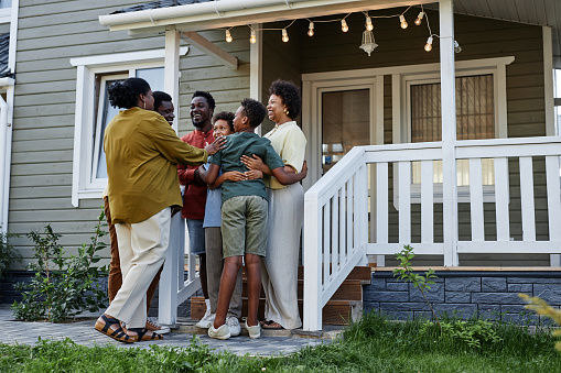 Full length portrait of happy black family embracing while standing on porch of new house, copy space