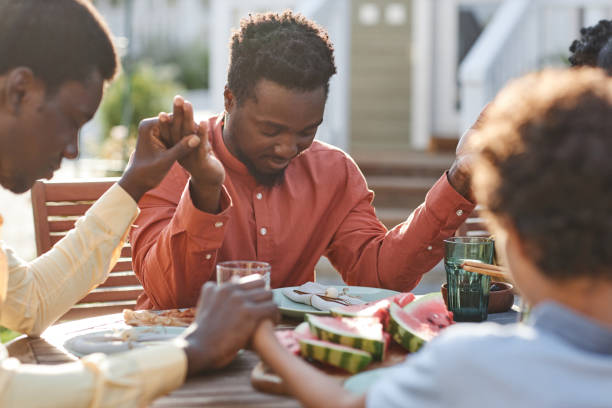 istock Young Man Saying Grace at Dinner Table Outdoors 1434816514