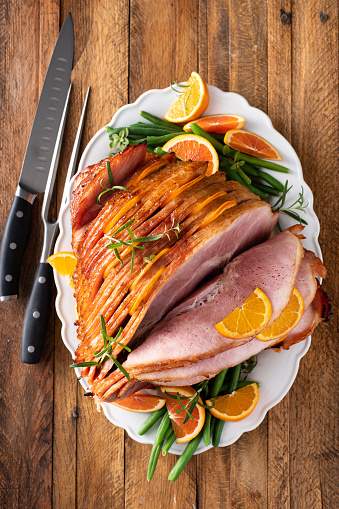 Christmas or Thanksgiving spiral sliced ham with oranges and herbs, whole ham on the serving plate