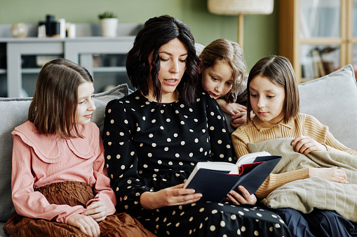 Portrait of young jewish mother reading book to three girls at home